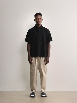 Standing model styling the black Kyneton Relaxed Fit Knit Polo A.B.C A BRAND COLLECTIVE boxy fit silhouette