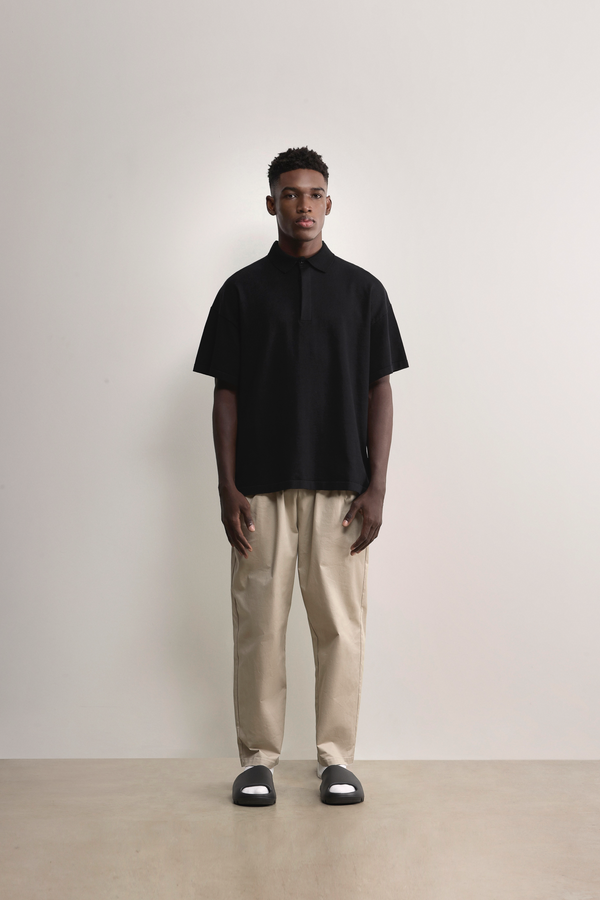 Standing model styling the black Kyneton Relaxed Fit Knit Polo A.B.C A BRAND COLLECTIVE boxy fit silhouette